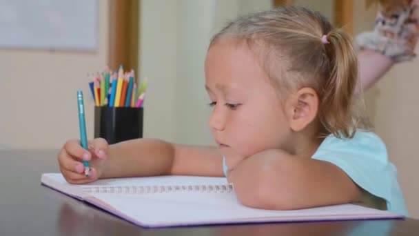 Menina bonito pouco senta-se em sala de aula e escrever em caderno de exercícios — Vídeo de Stock