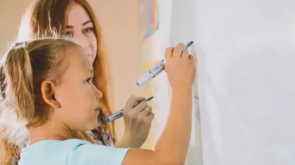 Lilla söta tjejen med läraren skriver på tavlan i klassrummet — Stockfoto