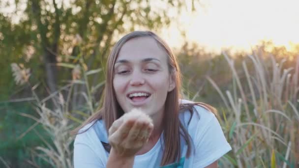 年轻的妇女的肖像是有乐趣吹蒲公英种子自然. — 图库视频影像
