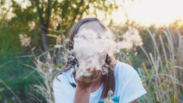 Retrato de mujer joven se divierte soplando semillas de diente de león en la naturaleza . — Vídeos de Stock