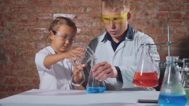 Мужчина-ученый с маленькой школьницей проводит химический эксперимент вместе — стоковое видео