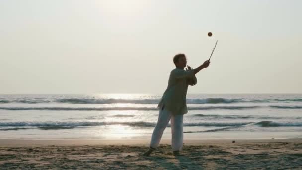 Starší žena cvičí tai chi míč balon na pláži při západu slunce — Stock video