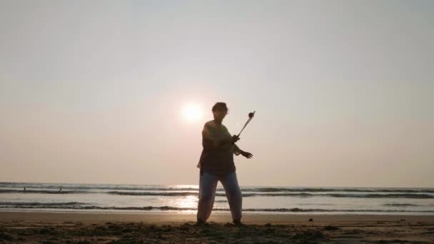 Femeie în vârstă care practică mingea de balon tai chi pe plajă la apusul soarelui — Videoclip de stoc
