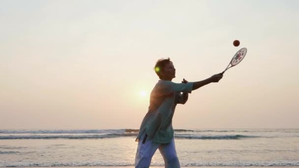 Femme âgée pratiquant le ballon de ballon tai chi sur la plage au coucher du soleil — Video