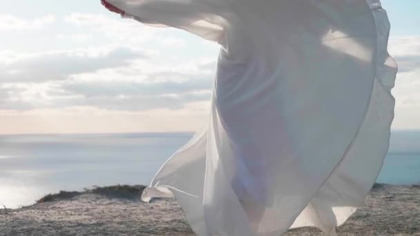 Smiling young woman in white dress is spinning around on the cliff — Stock Video