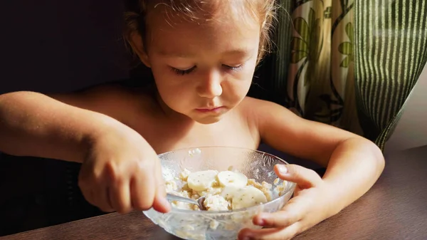 The child is having breakfast. Portrait of little cute girl eats porridge. — Stock Photo, Image