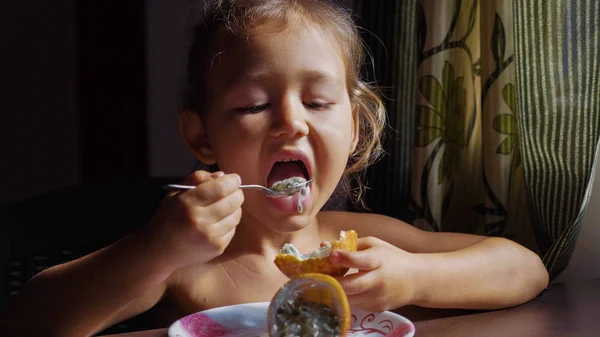 The child is having breakfast. Portrait of little cute girl eats passion fruit. — Stock Photo, Image