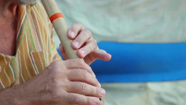 Senior mannen spelar bambu flöjt på stranden bredvid fiskebåt — Stockvideo