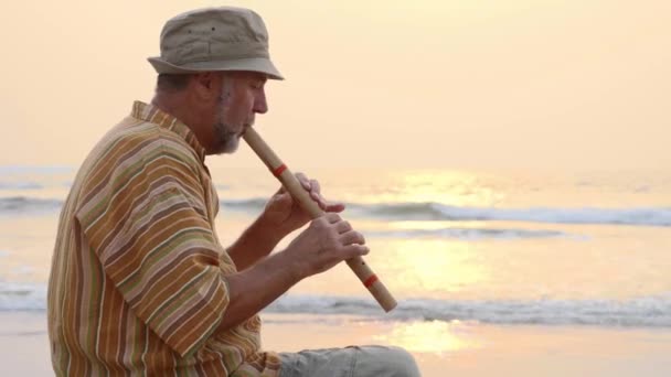 Homem sênior tocando flauta de bambu na praia ao pôr do sol — Vídeo de Stock