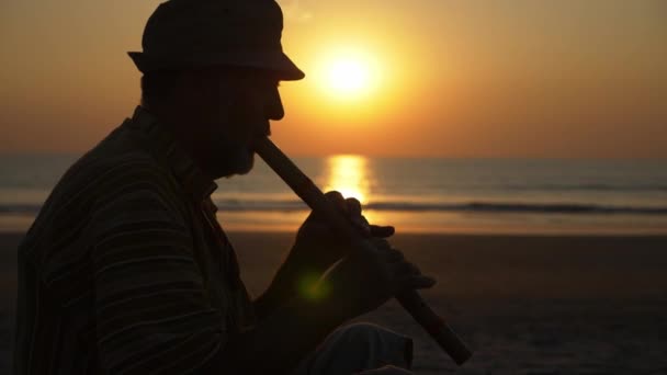 Silhouette of senior man playing bamboo flute on the beach at sunset — Stock Video