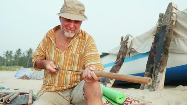 Homme âgé assis sur la plage et faisant flûte par les mains . — Video