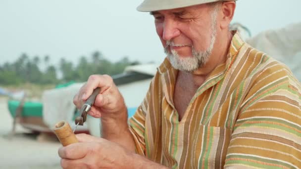 Senior man zit op het strand en maken fluit door handen, close-up. — Stockvideo