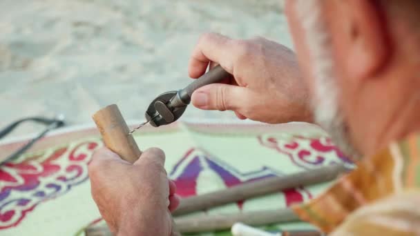Senior-Mann sitzt am Strand und macht Flöte mit den Händen, Nahaufnahme. — Stockvideo