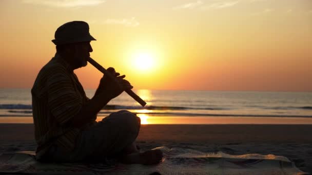 Silhouette d'homme âgé jouant de la flûte de bambou sur la plage au coucher du soleil — Video