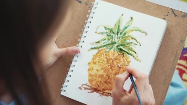 Close-up of female hand with paintbrush is drawing a pineapple by watercolors — Stock Video