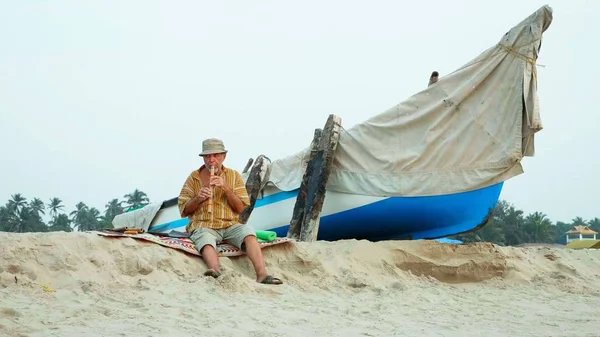 Hombre mayor tocando la flauta de bambú en la playa junto al barco de pesca — Foto de Stock