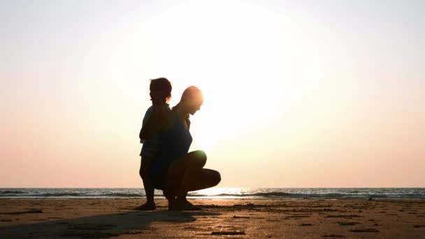 Silhouet van moeder met dochter gymnastische doen op het strand bij zonsondergang — Stockvideo
