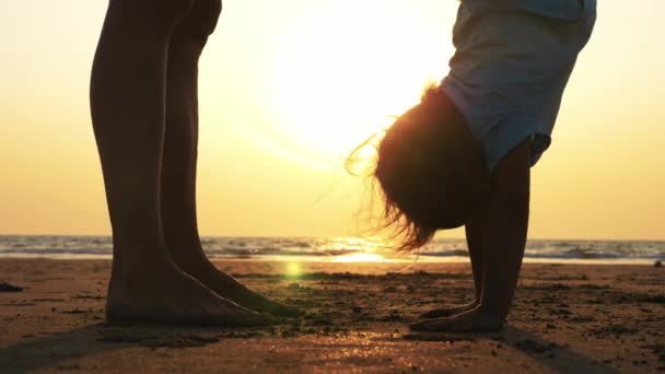 Silueta de madre con hija haciendo gimnasia en la playa al atardecer — Vídeo de stock