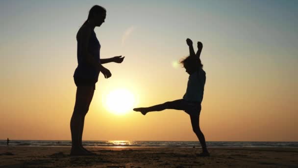 Silhuetten av mor med dotter gör gymnastik på stranden vid solnedgången — Stockvideo