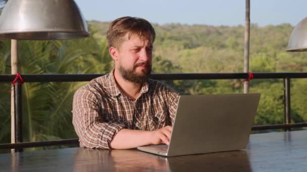 Hombre barbudo guapo escribiendo en el ordenador portátil al aire libre — Vídeo de stock