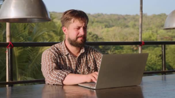 Hombre barbudo guapo escribiendo en el ordenador portátil al aire libre — Vídeos de Stock