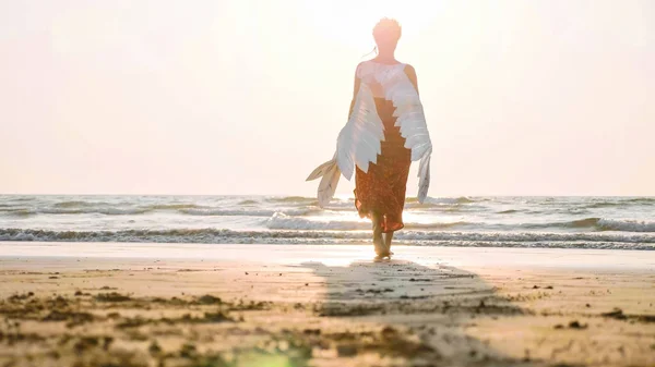 Krásný ženský anděl chůze naboso směrem k moři při západu slunce. — Stock fotografie