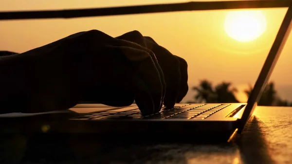 Close-up of silhouette male hands typing on laptop at beautiful sunset
