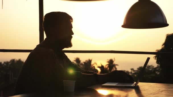 Silhouette dell'uomo barbuto che apre il computer portatile e inizia a lavorare all'aperto — Video Stock