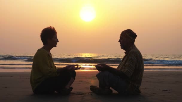 Casal sênior senta e meditando juntos na praia de areia — Vídeo de Stock