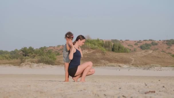 Jovem Sporty mãe com filhinha fazendo ginástica na praia . — Vídeo de Stock