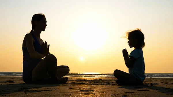 Silueta de madre con hija pequeña meditando juntos al atardecer —  Fotos de Stock