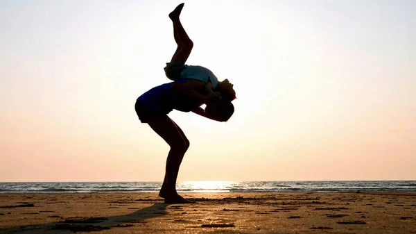 Silueta matky s dcerou dělá gymnastiku na pláži při západu slunce — Stock fotografie