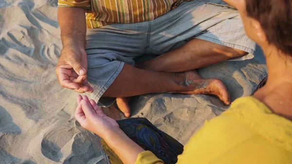 Урожай пожилой пары сидит и медитирует вместе на песчаном пляже — стоковое фото