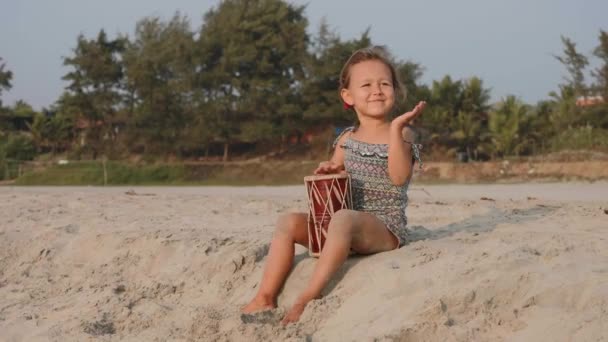 Petite fille mignonne jouant de la batterie sur une plage de sable . — Video