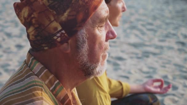 Senior couple sits and meditating together on sandy beach — Stock Video