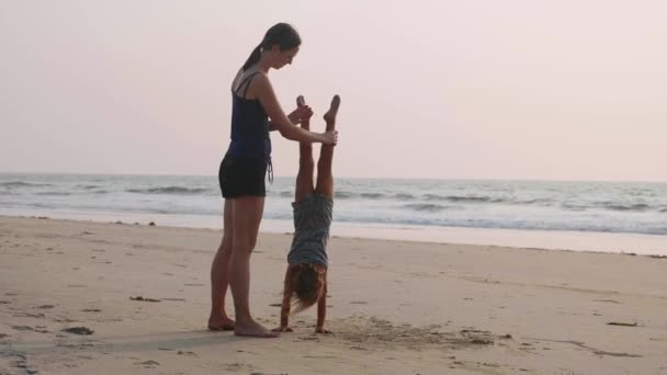 Mladý sportovní matka s malou dcerou dělá gymnastiku na pláži. — Stock video