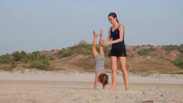 Sportig ung mor med lilla dotter gör gymnastik på stranden. — Stockvideo