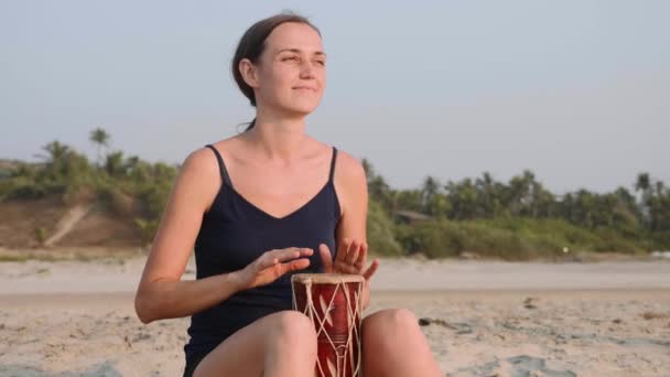 Young cheerful woman playing drums on sandy beach in slow motion. — Stock Video