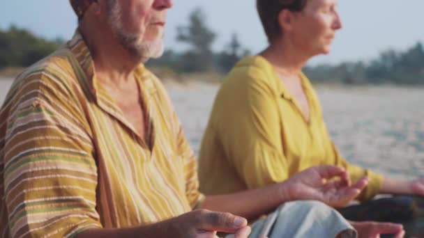 Starší pár sedí a společně meditoval na písečné pláži — Stock video