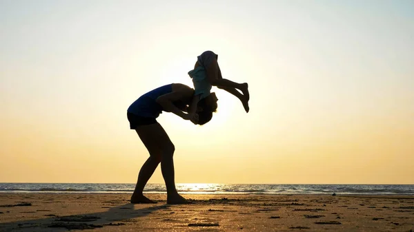 Silhouette of mother with daughter doing gymnastic on the beach at sunset