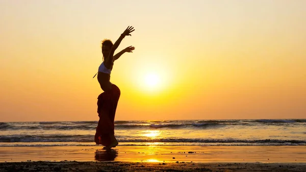 Silhueta de menina dançando na praia ao pôr do sol — Fotografia de Stock