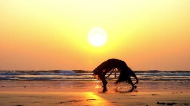 Güzel gün batımında sahilde jimnastik köprü yaparken Genç sportif kadın silüeti