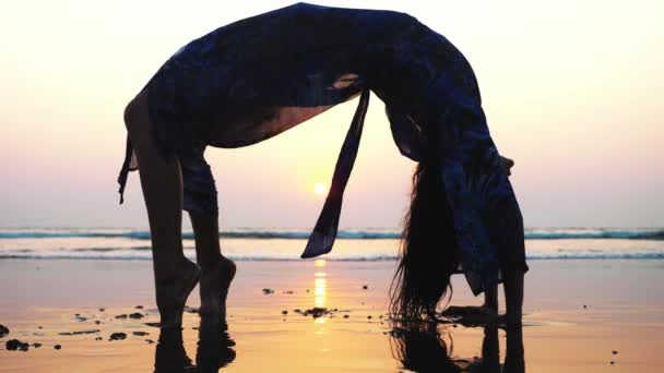 Silhuetten av ung kvinna gör gymnastiska bridge på stranden — Stockvideo