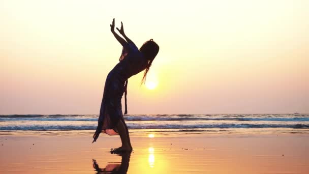 Silhouet van een jonge vrouw doet gymnastische brug op het strand — Stockvideo