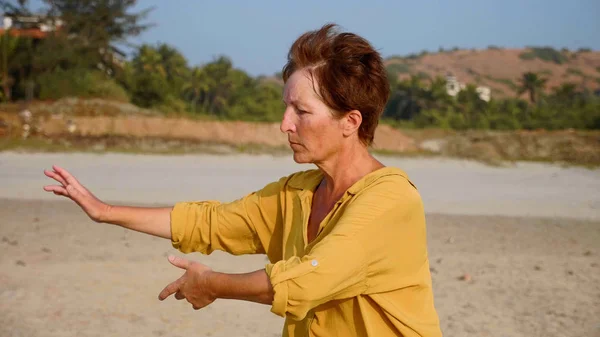 Старшая женщина практикует тайдзи гимнастику на песчаном пляже — стоковое фото