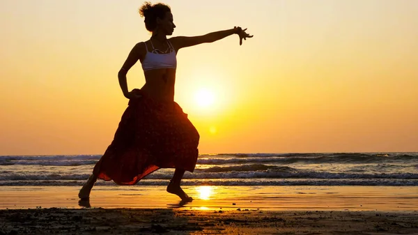 Silhueta de menina dançando na praia ao pôr do sol — Fotografia de Stock