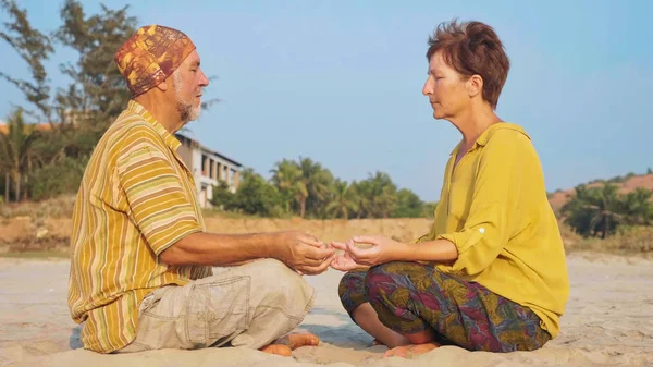 Старшая пара сидит и медитирует вместе на песчаном пляже — стоковое фото