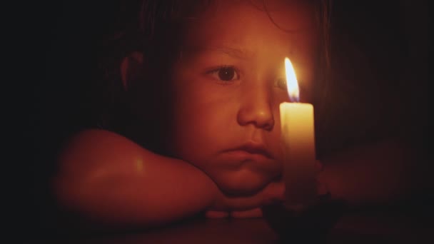 Ritratto bambina carina che si siede nel buio e guardando candela accesa — Video Stock