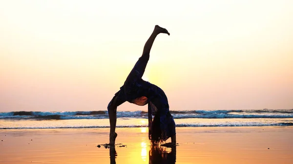 Silueta mladá žena, která dělá gymnastický můstek na pláži — Stock fotografie