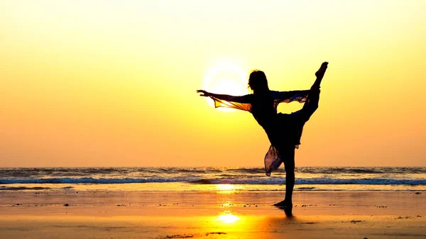 Силуэт молодой женщины, исполняющей элементы художественной гимнастики на пляже — стоковое фото